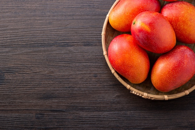 Fruta de mango fresca y hermosa en una canasta de bambú sobre un fondo de madera oscura, espacio de copia (espacio de texto), espacio en blanco para texto, vista superior.