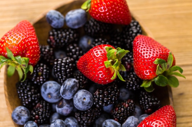 Fruta mixta fresca orgánica en un tazón de madera sobre la mesa.