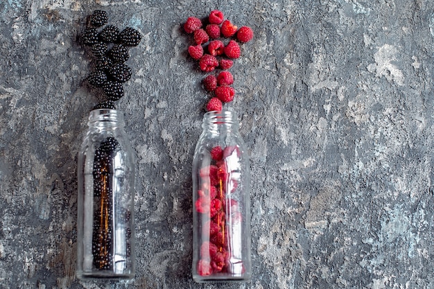 Fruta de moras y frambuesas en botellas de vidrio