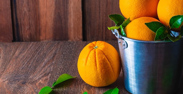 Fruta naranja fresca sobre una mesa de madera y muchas naranjas en una cesta de acero inoxidable sobre fondo de madera