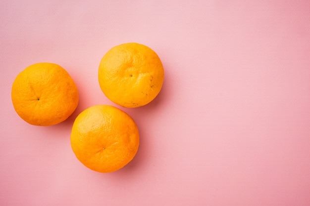 Fruta naranja orgánica fresca, sobre fondo de verano con textura rosa, vista superior plana, con espacio para copiar texto