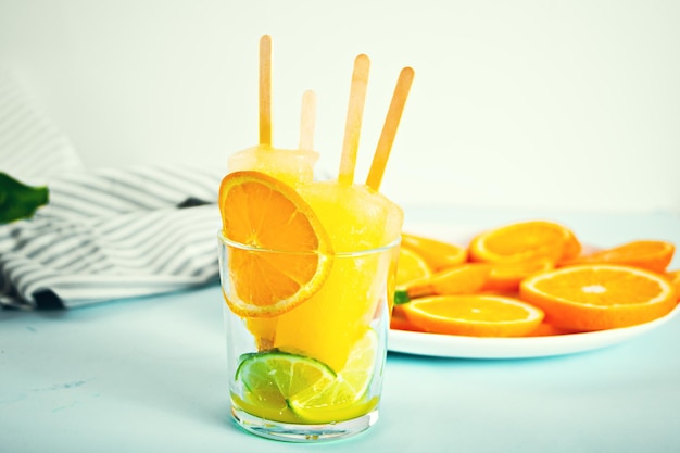 Fruta naranja paletas cítricas paletas heladas en vidrio y rodajas de naranja en un plato en el fondo