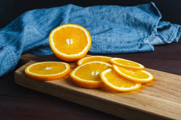 Fruta de naranjas en rodajas cerca de textil de mezclilla en tablero de madera Concepto mínimo de cítricos de frutas jugosas de naranja