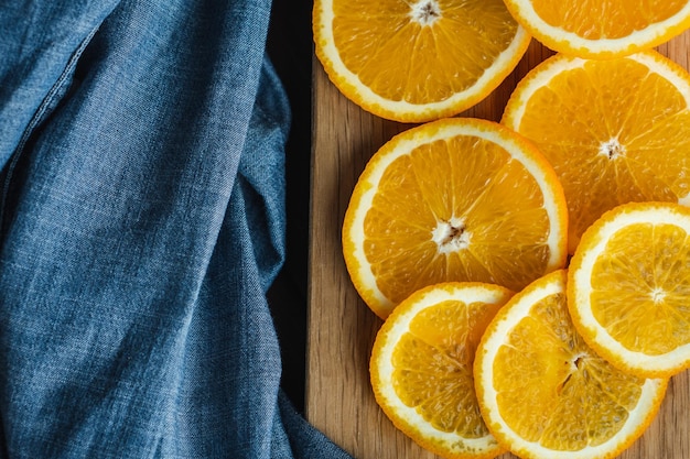 Fruta de naranjas en rodajas cerca de textil de mezclilla en tablero de madera Concepto mínimo de cítricos de frutas jugosas de naranja