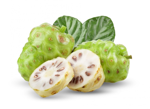 Fruta de noni con hojas en mesa blanca.