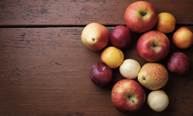 Fruta de otoño en una mesa de madera Manzanas peras ciruelas albaricoques sobre un fondo rojo oscuro