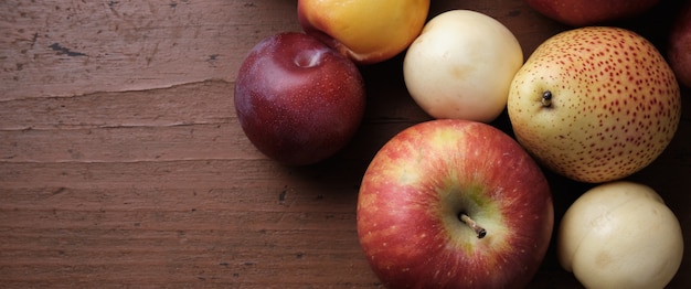 Fruta de otoño en una mesa de madera Manzanas peras ciruelas albaricoques sobre un fondo rojo oscuro