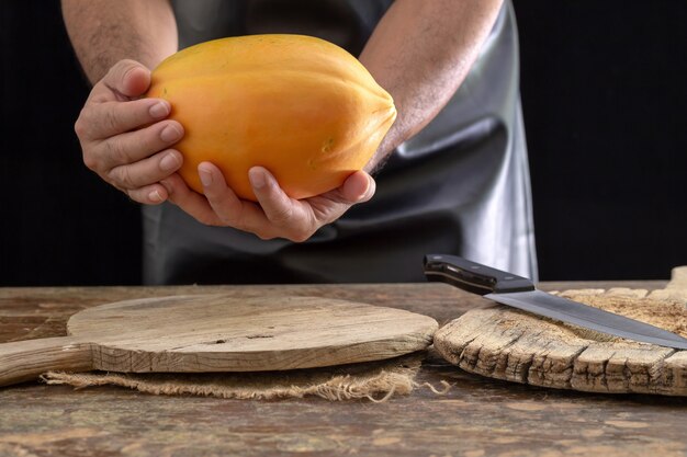 Foto fruta de papaya madura en manos de hombres sobre fondo de madera