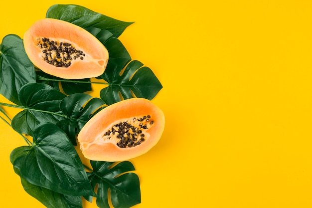 Fruta de papaya a la mitad con hojas verdes artificiales sobre fondo amarillo