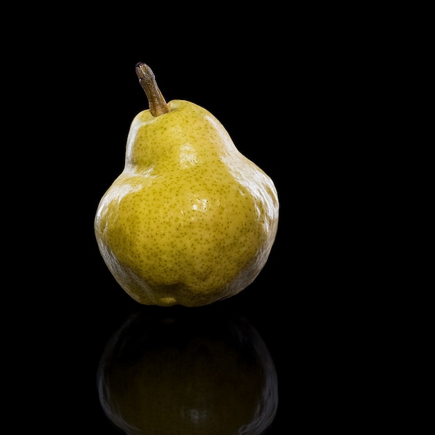 Foto fruta de pera amarilla madura, con reflejo en superficie negra, aislada en negro