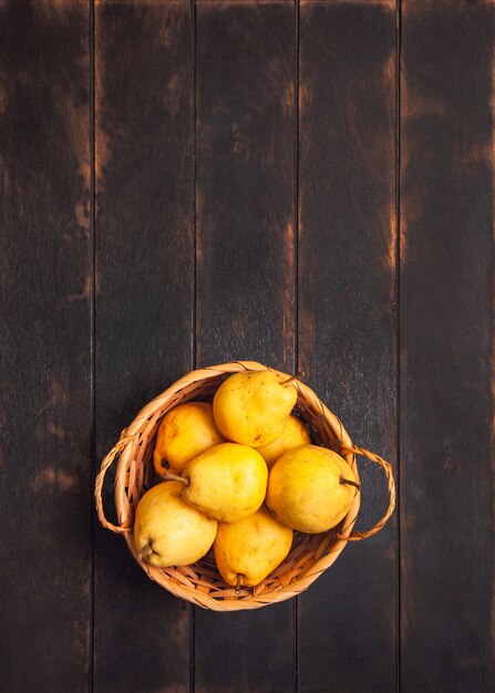 Fruta de pera natural con defectos en la canasta sobre fondo de madera oscura.