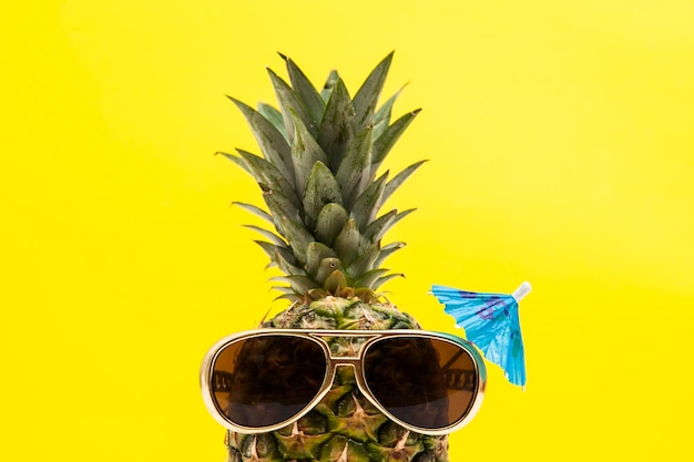 Fruta de piña de verano con gafas de sol contra un fondo amarillo brillante