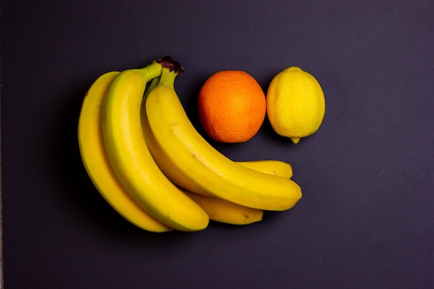 Fruta sobre fondo negro. Plátanos, limón y naranja sobre fondo negro. Frutos brillantes.