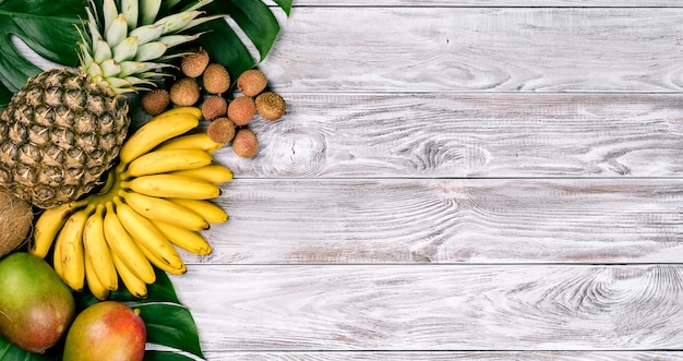 Fruta tropical fresca en la vista superior de madera. plátanos, piña, coco, mango, lichi, castañas.