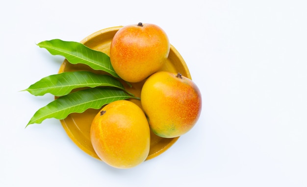 Fruta tropical, mango en placa amarilla sobre superficie blanca. Vista superior