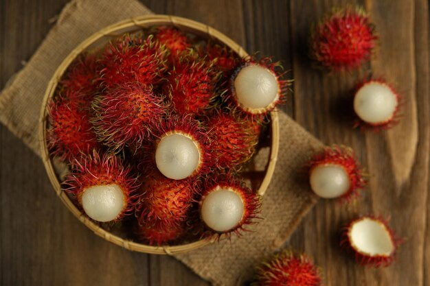 Foto fruta tropical rambután fresca en una cesta con fondo de madera