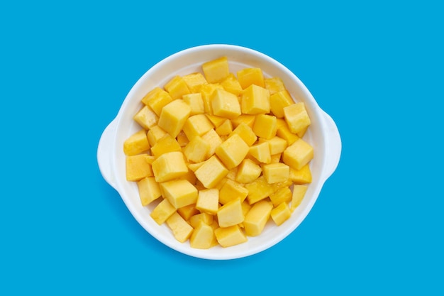Fruta tropical, rodajas de cubo de mango en tazón blanco sobre fondo azul.