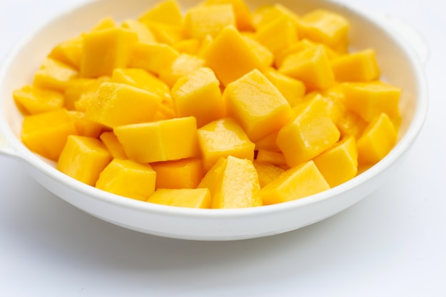 Fruta tropical, rodajas de cubo de mango en un tazón blanco sobre fondo blanco.