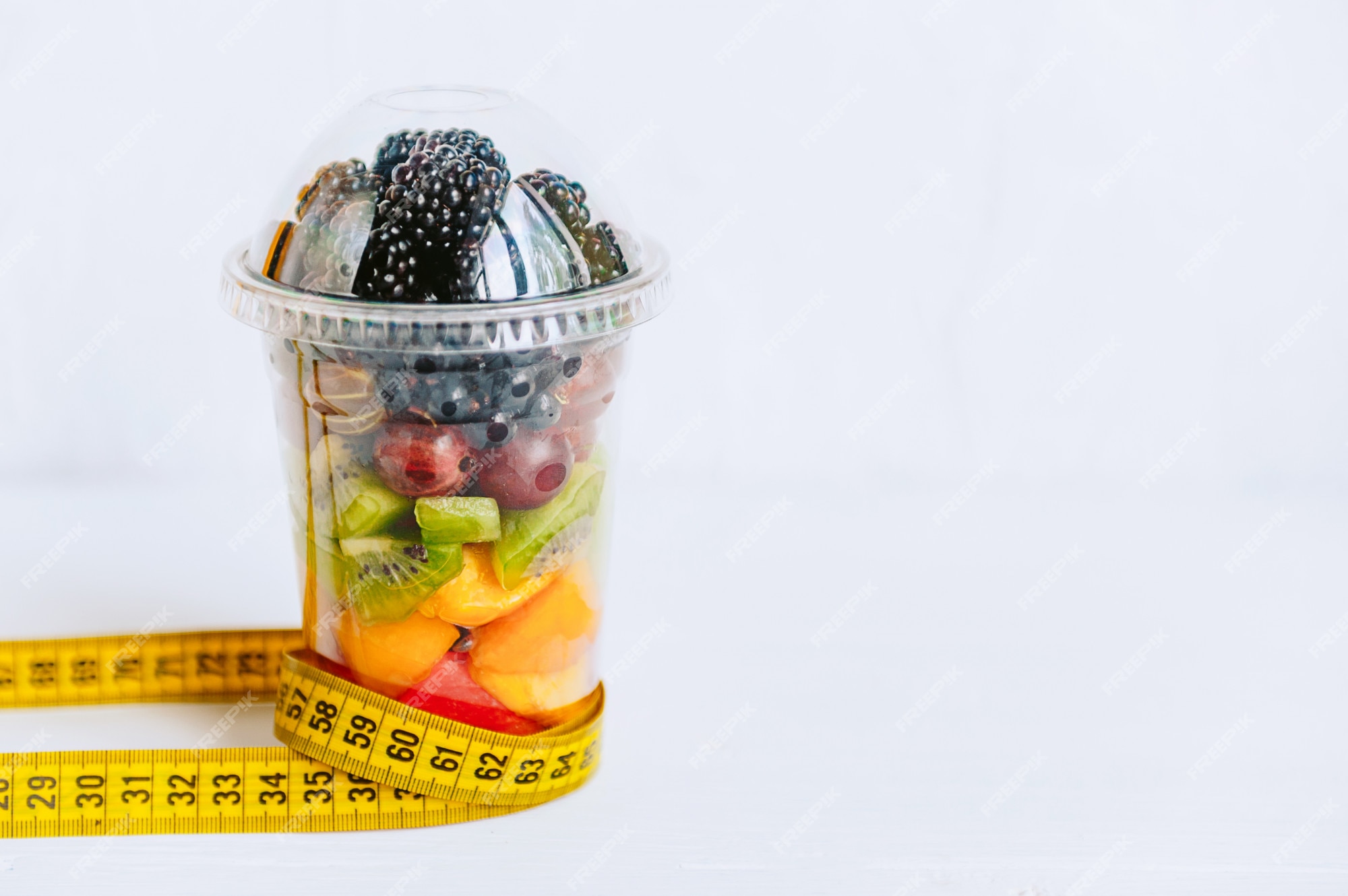Fruta en un vaso y una cinta para medir el cuerpo.