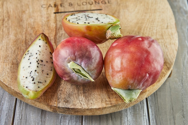 Frutas de cactus de manzana peruana enteras y cortadas en soporte de madera sobre tablero gris. Nombre científico Cereus repandus