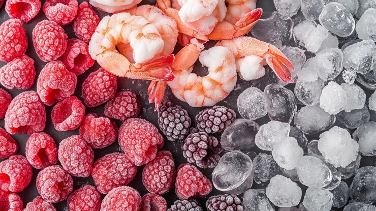 Frutas y camarones congelados dispuestos en patrones coloridos en una superficie negra