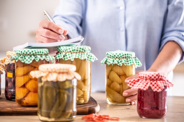 Frutas caseiras em conserva e vegetais em conserva com uma mulher escrevendo a receita no fundo.