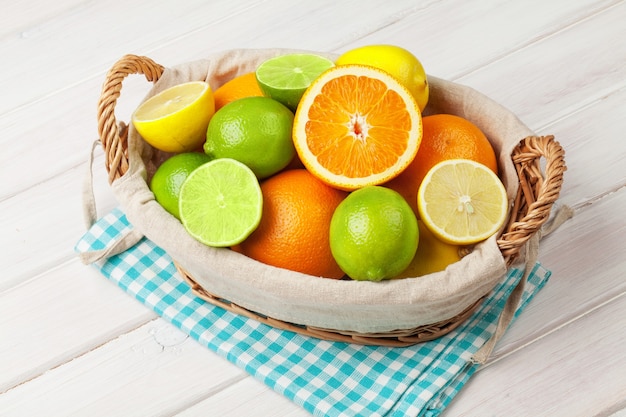 Frutas cítricas en canasta. Naranjas, limas y limones. Sobre fondo de mesa de madera blanca