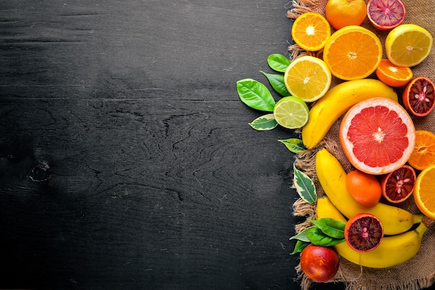 Frutas cítricas frescas limão laranja tangerina limão em um fundo preto vista superior de madeira