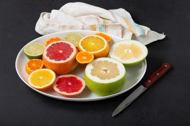 Frutas cítricas frescas en un plato blanco de cerca, fondo oscuro