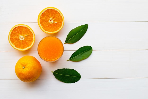 Frutas cítricas naranjas frescas con hojas y jugo de naranja sobre madera blanca