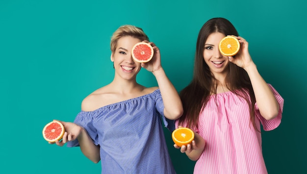 Frutas cítricas para o cuidado da pele. duas mulheres sorridentes segurando laranja e toranja no rosto.