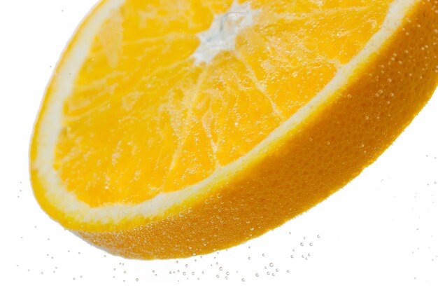 Frutas, comida y concepto de alimentación saludable: cierre de una rodaja de naranja fresca que cae o se sumerge en agua con salpicaduras sobre fondo blanco