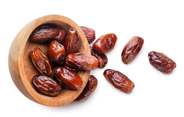 Frutas de dátiles derramadas de un plato de madera sobre un fondo blanco Vista superior