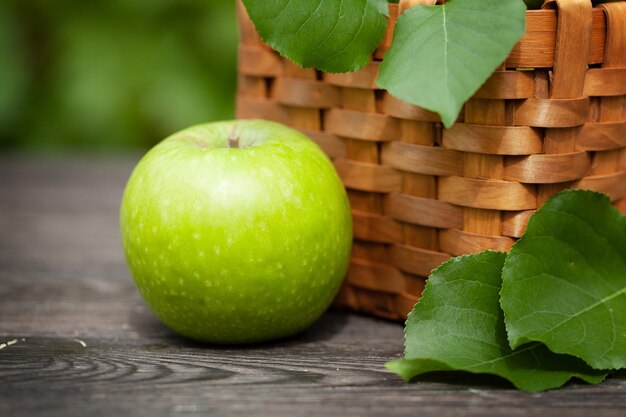 Frutas de maçã verde em uma cesta em uma mesa de jardim ensolarada