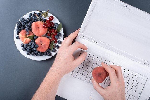 Frutas de verão em um fundo cinza com um laptop em pêssegos e cerejas de tinta branca