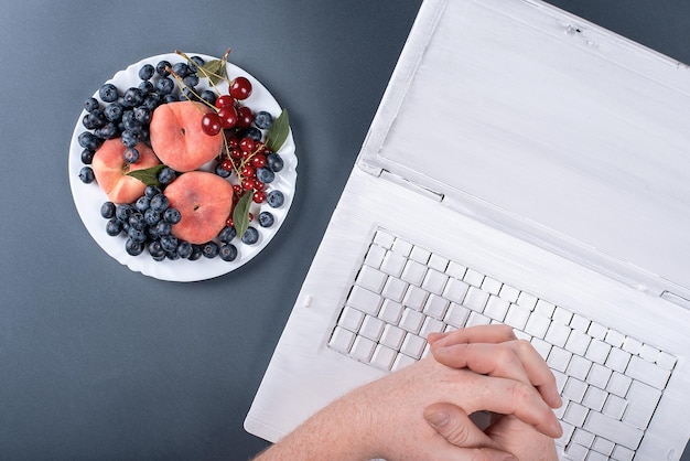 Frutas de verão em um fundo cinza com um laptop em pêssegos e cerejas de tinta branca