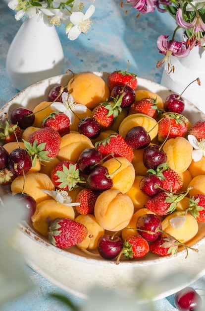 Frutas e frutas frescas maduras - damascos, morangos, cerejas em um prato com gotas de água sobre um fundo azul