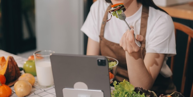 Frutas e vegetais deliciosos em uma mesa e mulher cozinhando A dona de casa está cortando pepinos verdes em uma tábua de madeira para fazer salada fresca na cozinha