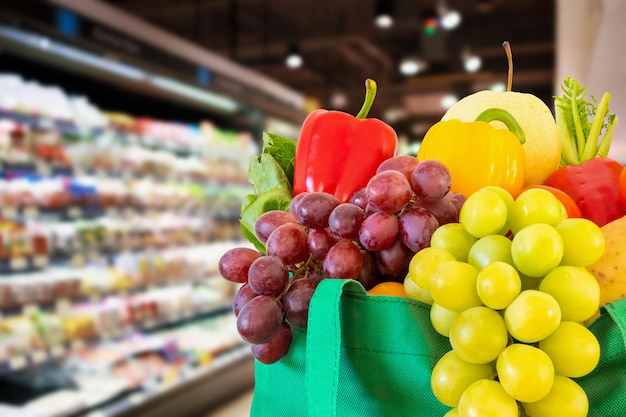 Frutas e vegetais frescos em sacola de compras verde reutilizável com fundo de mercearia de supermercado