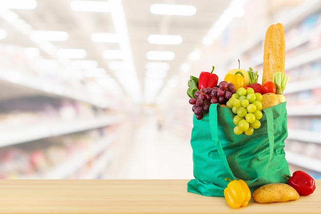 frutas e vegetais na sacola de compras na mesa de madeira com fundo de mercearia de supermercado