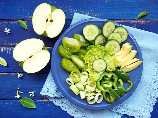 Frutas e vegetais verdes - alho-poró, pepino, salada de alface, abacate, maçã e pimenta verde na mesa de madeira azul