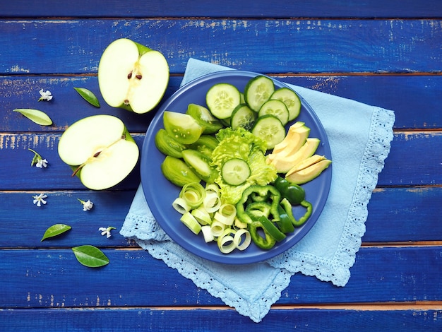 Frutas e vegetais verdes - alho-poró, pepino, salada de alface, abacate, maçã e pimenta verde na superfície de madeira azul