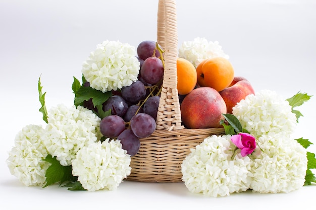 Frutas em um prato são pêssegos e grandes uvas pretas Cesta com um buquê de hortênsias