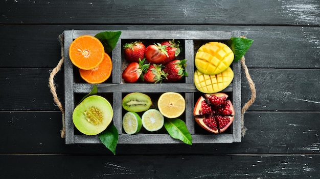Foto frutas em uma caixa de madeira. citrus, melão, romã, morango, banana. vista do topo. espaço livre para o seu texto.