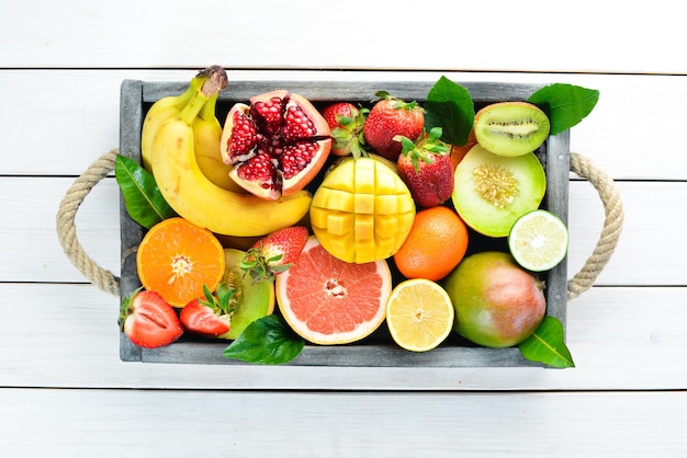 Frutas em uma caixa de madeira. Citrus, melão, romã, morango, banana. Vista do topo. Espaço livre para o seu texto.