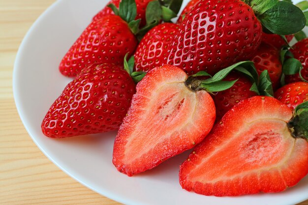 Frutas enteras y secciones transversales de frutas de fresa maduras frescas rojas vibrantes en un plato blanco