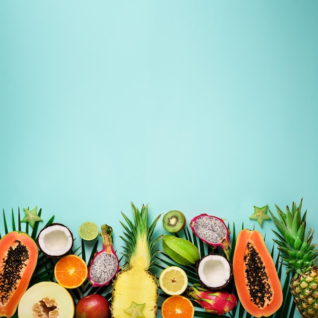 Foto frutas exóticas e folhas de palmeira tropical em fundo pastel turquesa mamão manga abacaxi banana carambola fruta do dragão kiwi limão laranja melão coco limão vista superior