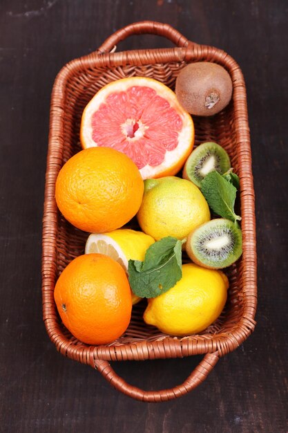 Foto frutas exóticas frescas con hojas verdes en una canasta de mimbre sobre fondo de madera