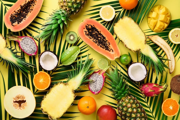 Foto frutas exóticas y hojas de palmeras tropicales sobre fondo amarillo pastel papaya mango piña plátano carambola fruta del dragón kiwi limón naranja melón coco lima vista superior