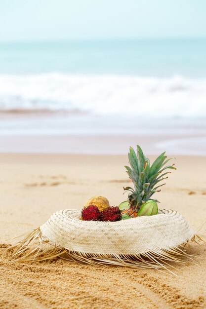 Frutas exóticas en un sombrero de paja cerca del océano.